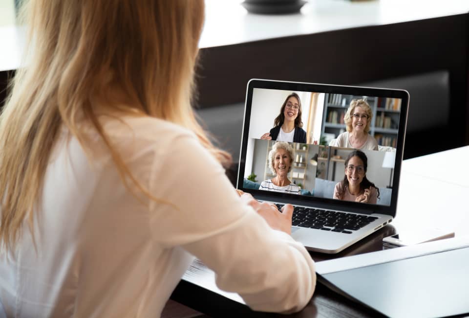 Blonde Frau sitzt vor ihrem Laptop und spricht in einer Videokonferenz mit 4 weiteren Personen