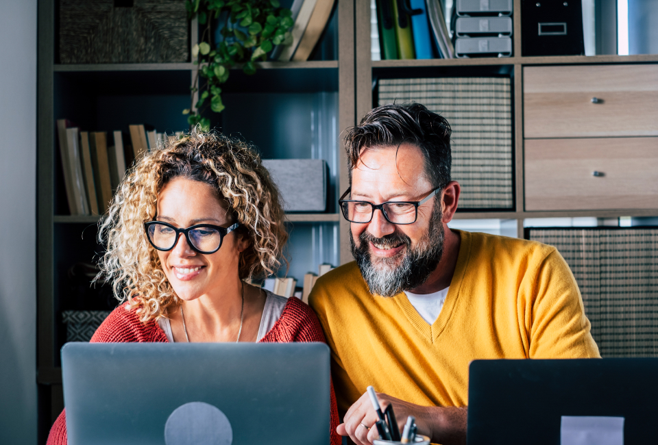Eine Frau und ein Mann sitzen lächelnd vorm Computer und lernen italienisch online