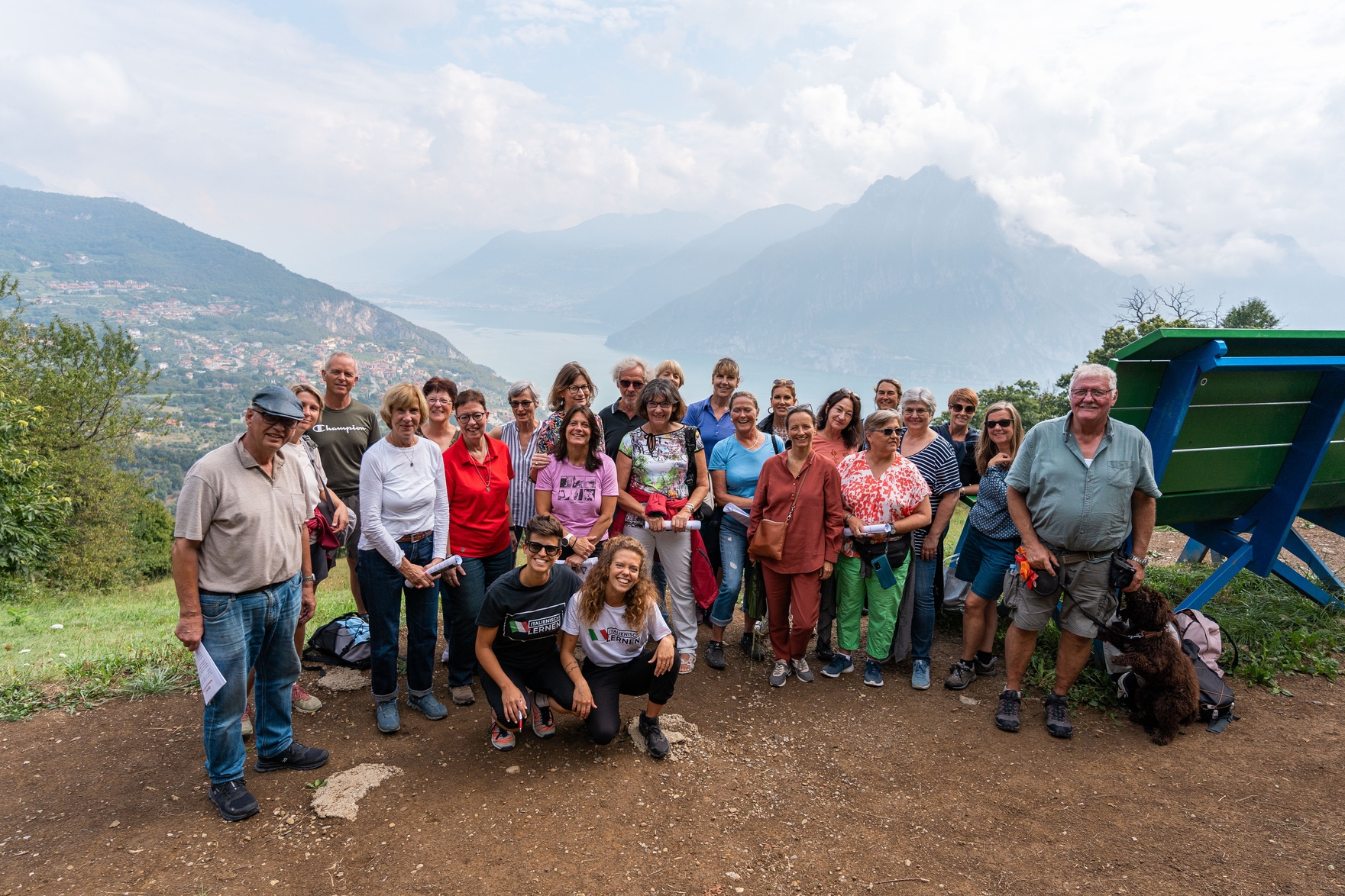 Eine Gruppe von Menschen posiert auf einem malerischen Hügel mit Bergen und einem See im Hintergrund.