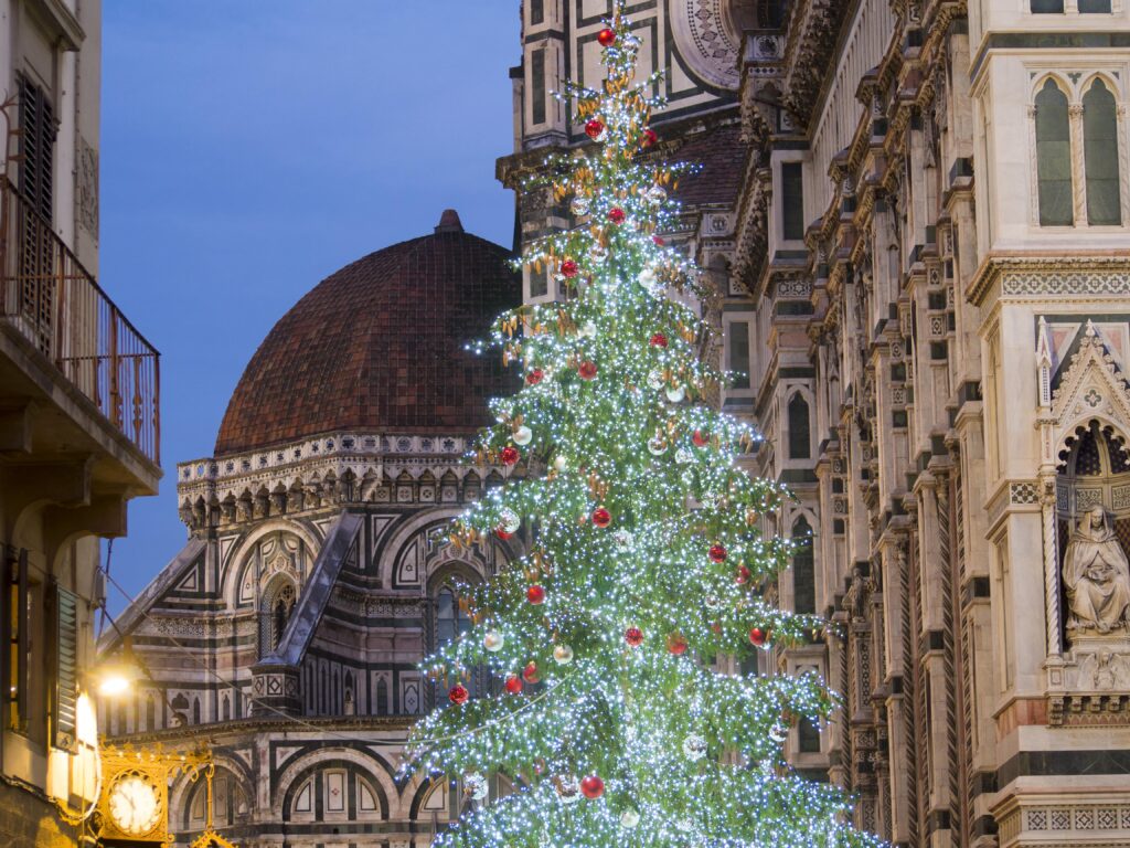 Ein großer, geschmückter Weihnachtsbaum mit Lichtern steht abends vor der Kathedrale von Florenz in Italien und schafft eine zauberhafte Weihnachtsszene.