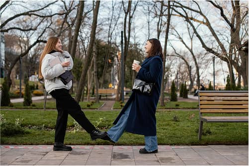 Zwei Frauen gehen durch einen Park mit kahlen Bäumen und Parkbänken