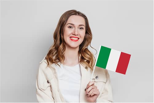 Lächelnde braunhaarige Frau in cremefarbenem Pullover hält kleine italienische Flagge