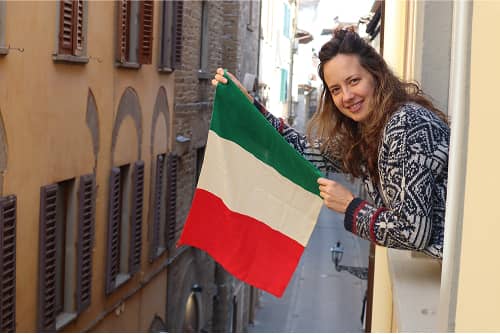 Frau mit lockigen Haaren hält italienische Flagge in schmaler mediterraner Gasse