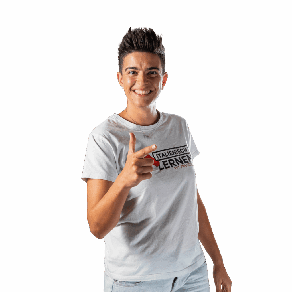 Person mit kurzen dunklen Haaren, die ein weißes "Italienisch Lernen Mit Francesca"-T-Shirt und Jeans trägt, lächelt und die "Non ce n'è"-Geste macht, indem sie in Richtung der Kamera zeigt, vor einem schlichten Hintergrund.