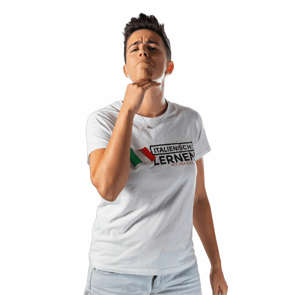 Eine Person mit kurzen Haaren in weißem T-Shirt und hellen Jeans, die die "Non mi importa"-Geste unter dem Kinn macht.