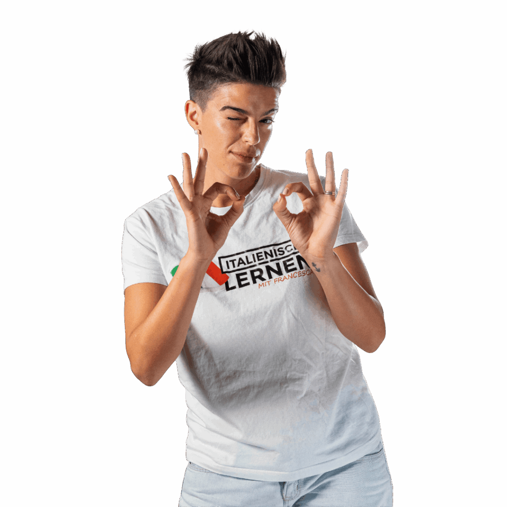 Person mit kurzen dunklen Haaren, die ein weißes "Italienisch Lernen Mit Francesca"-T-Shirt trägt, mit beiden Händen die "Perfetto"-Geste macht und zwinkert, vor einem schlichten Hintergrund stehend.