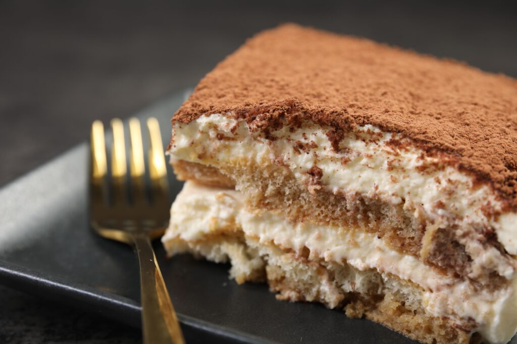 piece of tasty tiramisu and fork on black table, closeup