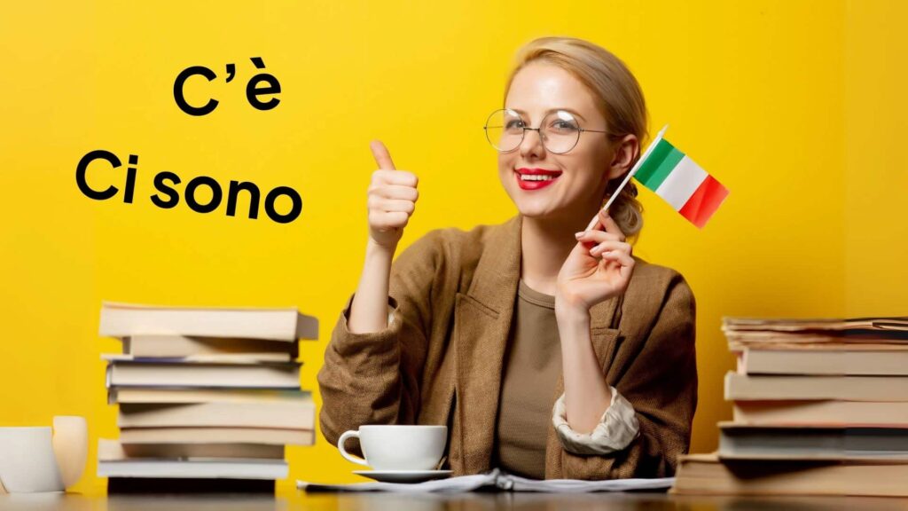 Lächelnde Frau mit blonden Haaren, die an einem Schreibtisch sitzt, umgeben von Stapeln von Büchern und eine kleine italienische Flagge hält.