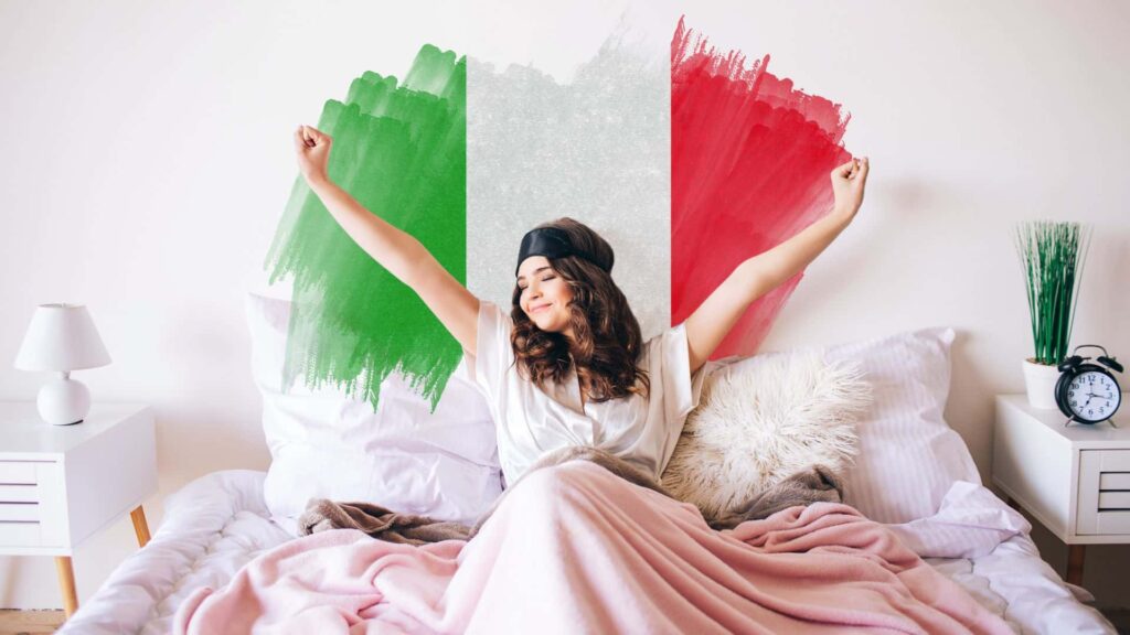 Ein Mädchen mit braunen Haaren streckt sich im Bett zwischen den Kissen, hinter ihr die italienische Flagge.