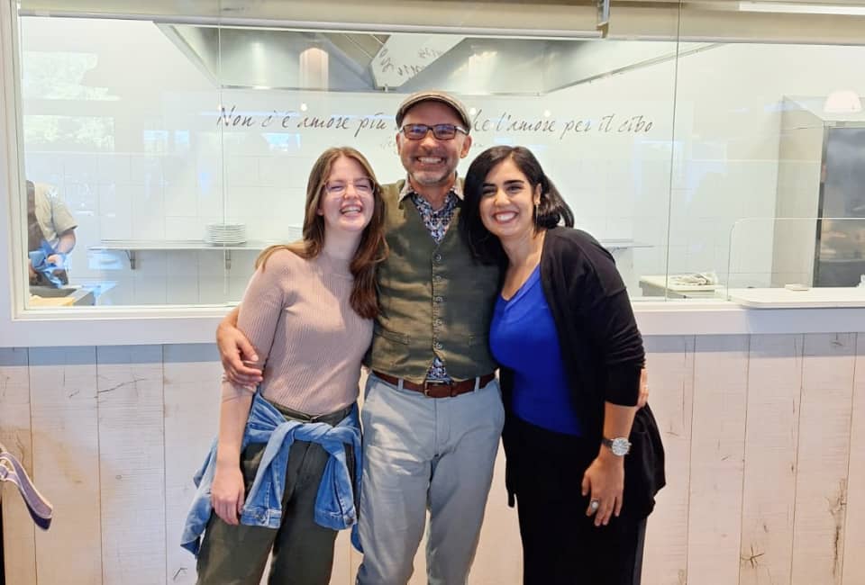 Drei lächelnde Personen in einem italienischen Café mit Nudelauslage im Hintergrund