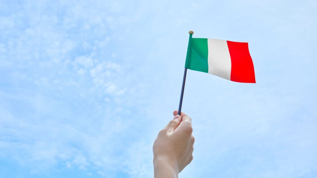 Eine Hand hält eine kleine italienische Flagge vor blauem Himmel.
