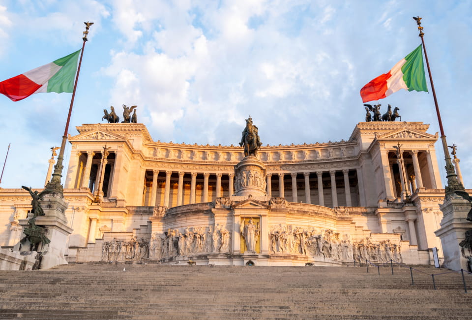 Der Altare della Patria in Rom, Italien, mit zwei italienischen Flaggen auf beiden Seiten des Denkmals und einer Treppe, die zum Eingang hinaufführt.